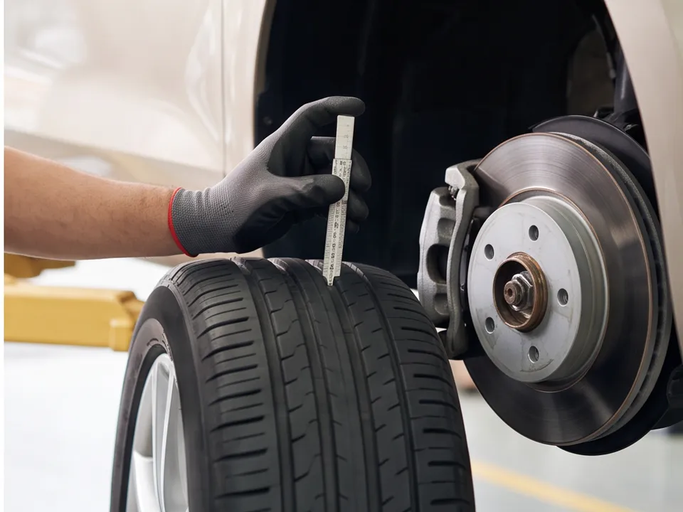 A mechanic's gloved hand measuring tyre tread depth next to a brake disc